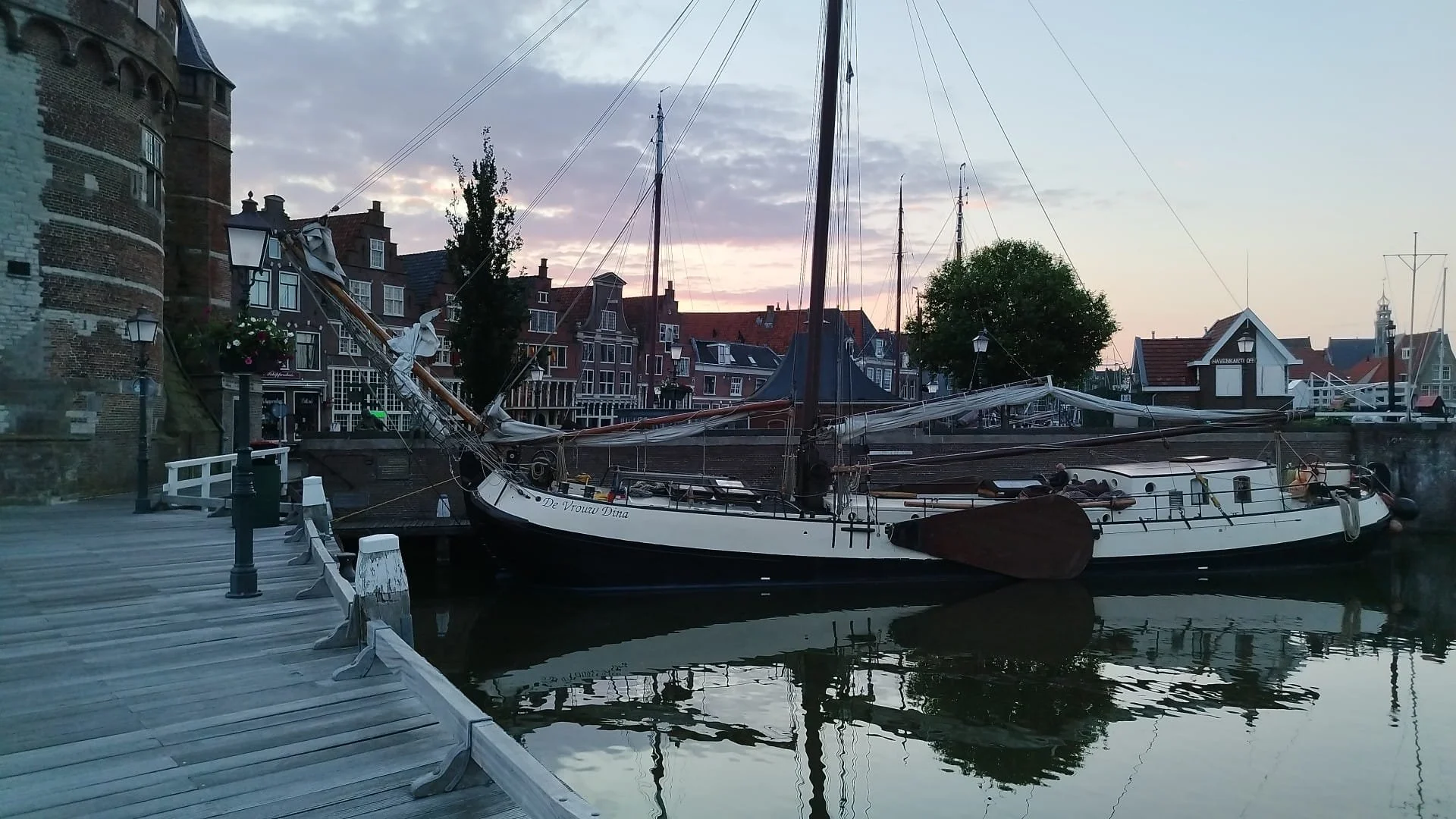 Traditioneel Nederlands zeilschip "De Vrouw Dina"  aangemeerd bij haven in Leiden, historische Nederlandse stad met oude gebouwen en brug.