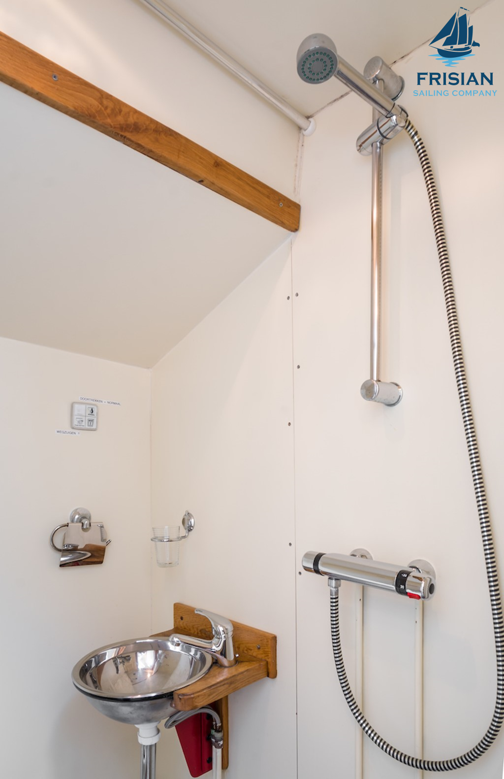 Kleine badkamer met een hangende douchekop, metalen wastafel en Frisians Sailing Company logo.