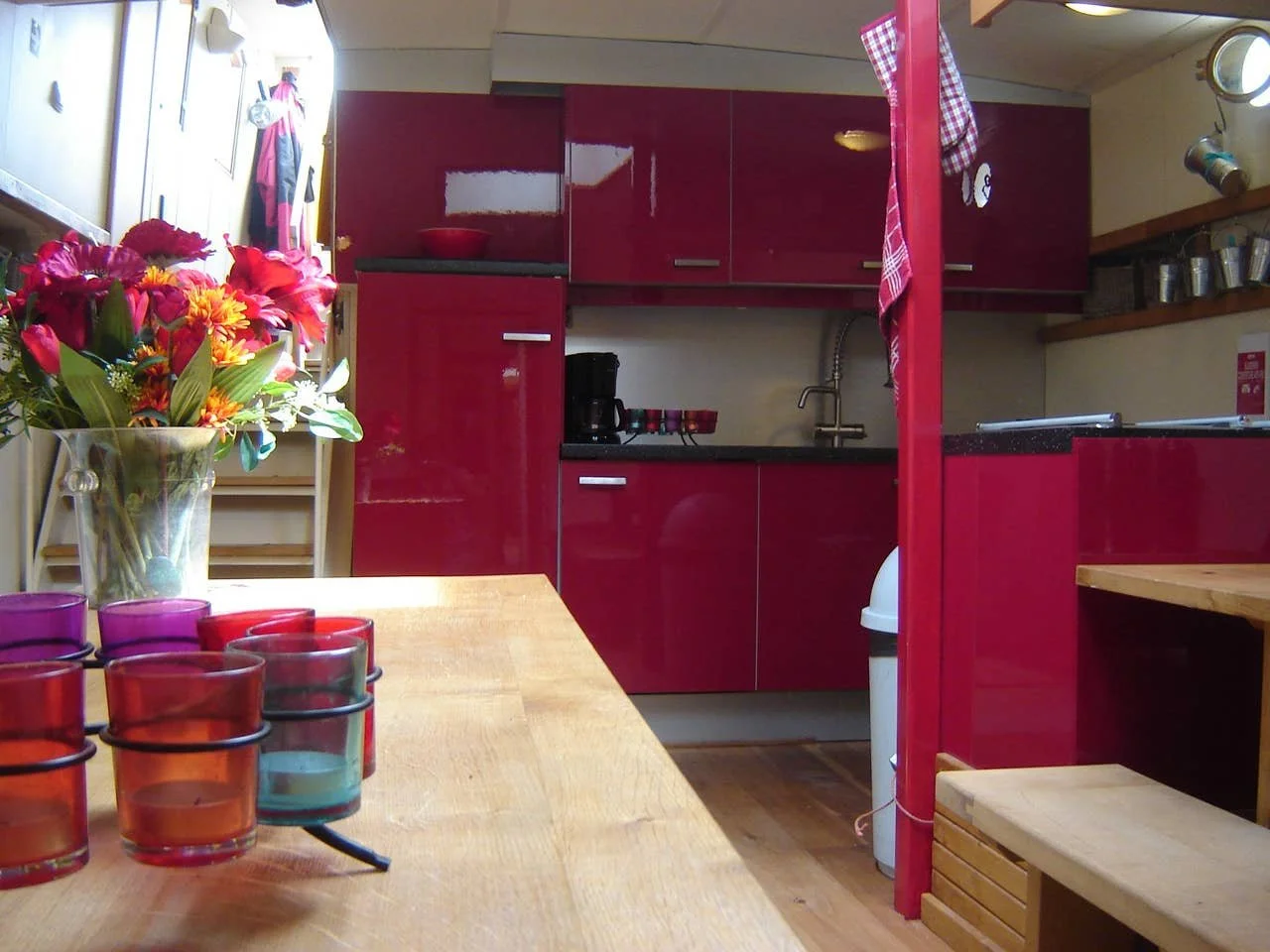 Keuken met rode kasten, houten tafel, glazen met kaarsen en een bloemenvaas.