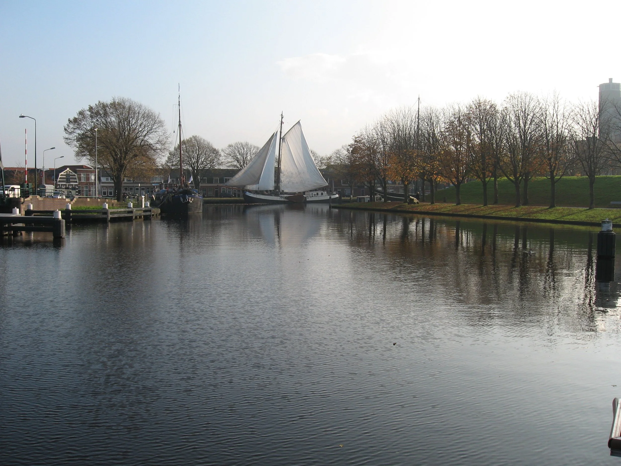 Kanaal met zeilboot en bomen in herfst.