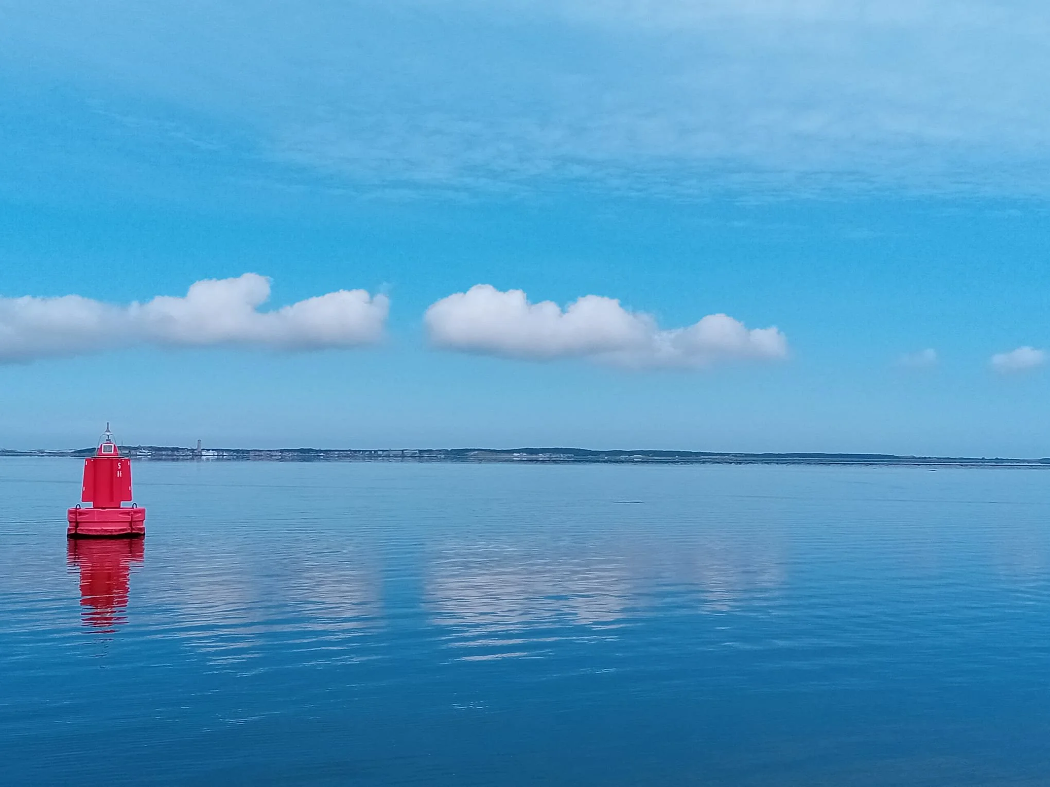 Rode boei op kalme zee onder blauwe hemel met wolken.
