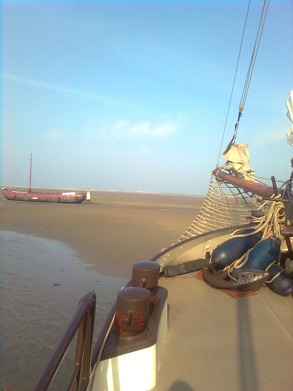 Een boot op een zandbank met bijboot en touwen, blauwe lucht op de achtergrond.