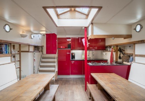 Keuken in een woonboot met rode kasten en houten meubels.