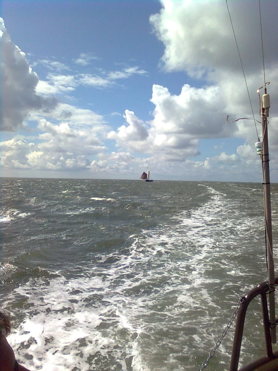 Zee met een zeilboot in de verte en bewolkte hemel.