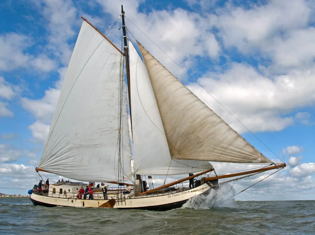 Traditioneel Nederlands zeilschip "De Vrouw Dina"  op zee met bemanning in actie, helderblauwe lucht en wolken.