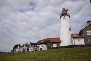 Vuurtoren op een heuvel bij een rij huizen onder een bewolkte hemel.