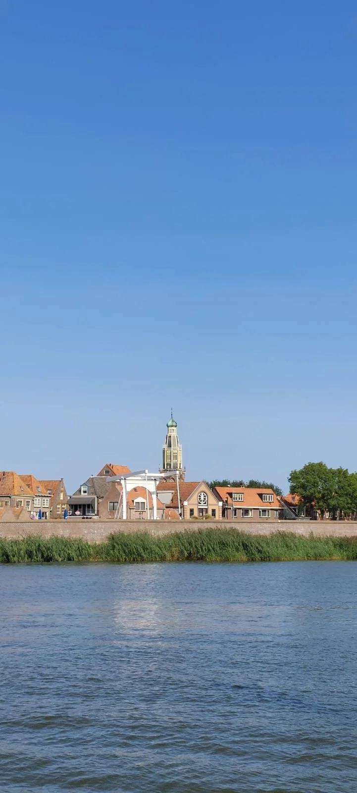 Rivier met houten huizen en een kerktoren op de achtergrond onder een blauwe lucht.