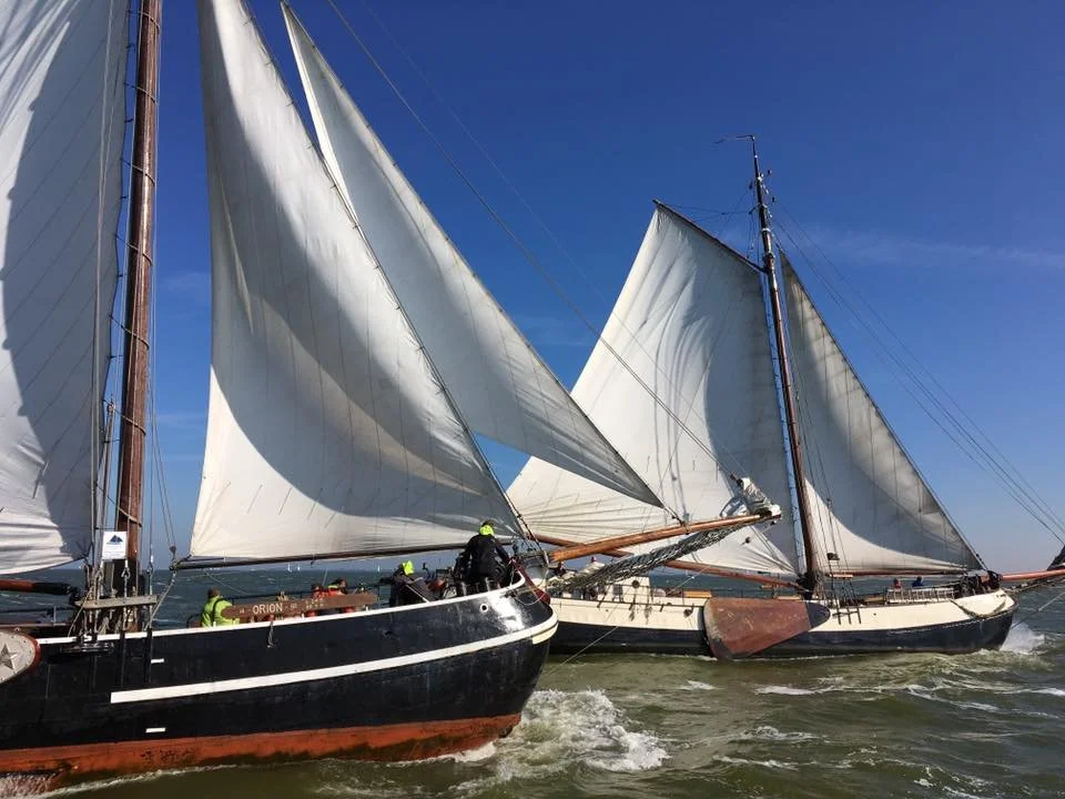 Twee zeilboten met volle zeilen op zee onder een blauwe lucht.