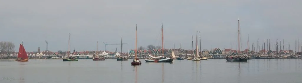 Panorama van een haven met traditionele zeilboten en huizen aan de waterkant.
