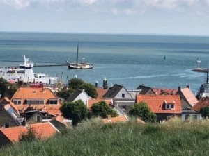 Uitzicht op een kustplaats met rode daken en een zeilboot op de achtergrond bij de zee.