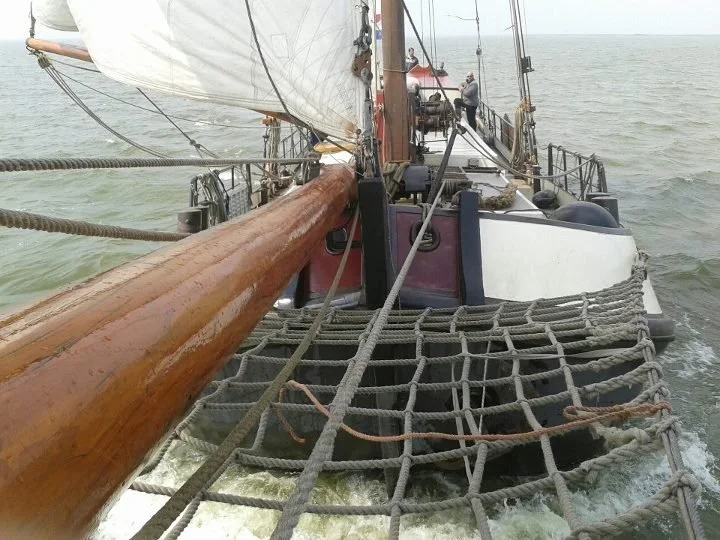 Zeedijk van een zeilboot met grootzeil en net over het water.