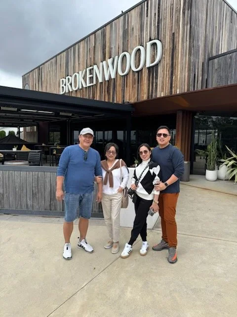 Four people standing in front of a wood-paneled building with a sign that says 'Brokenwood'.