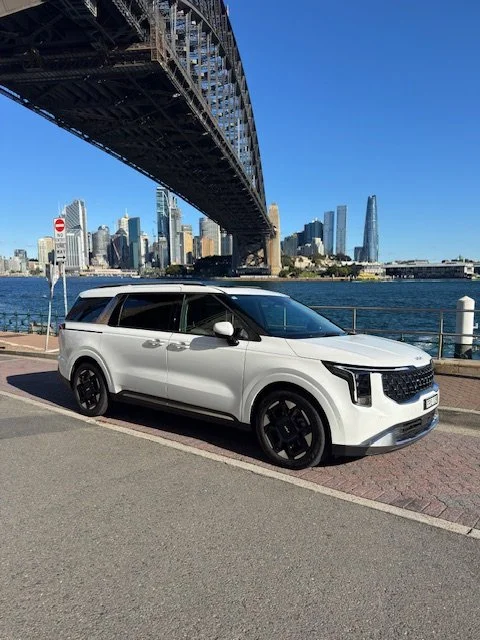 White SUV parked near Sydney Harbour with the Sydney Harbour Bridge and city skyline in the background.