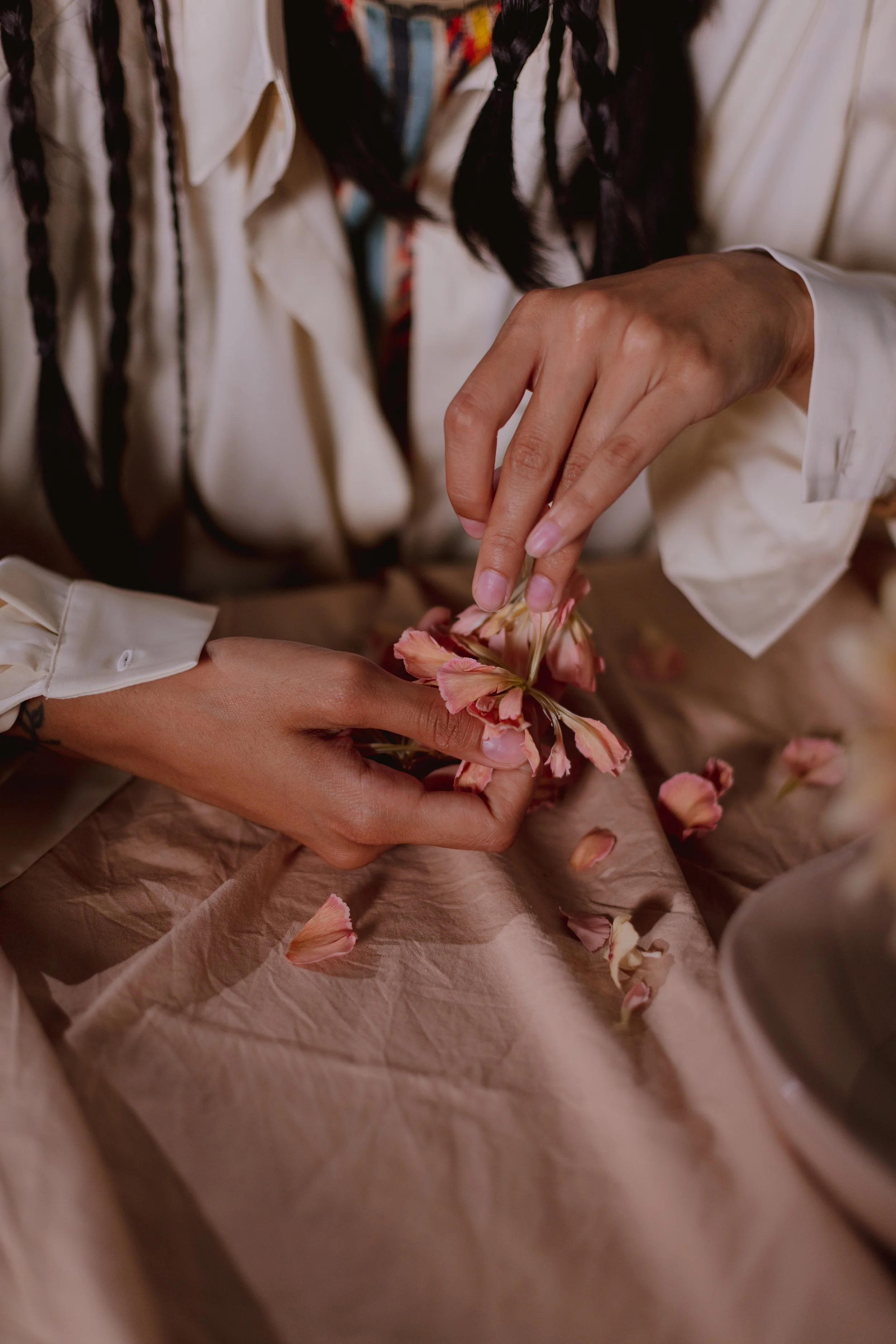 Manos deshojando flores rosadas sobre una tela clara.