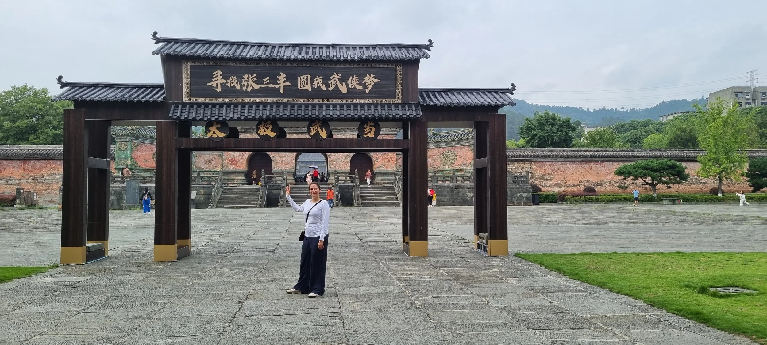 Tourist standing in front of traditional Chinese archway and temple entrance, surrounded by stone courtyard and trees.