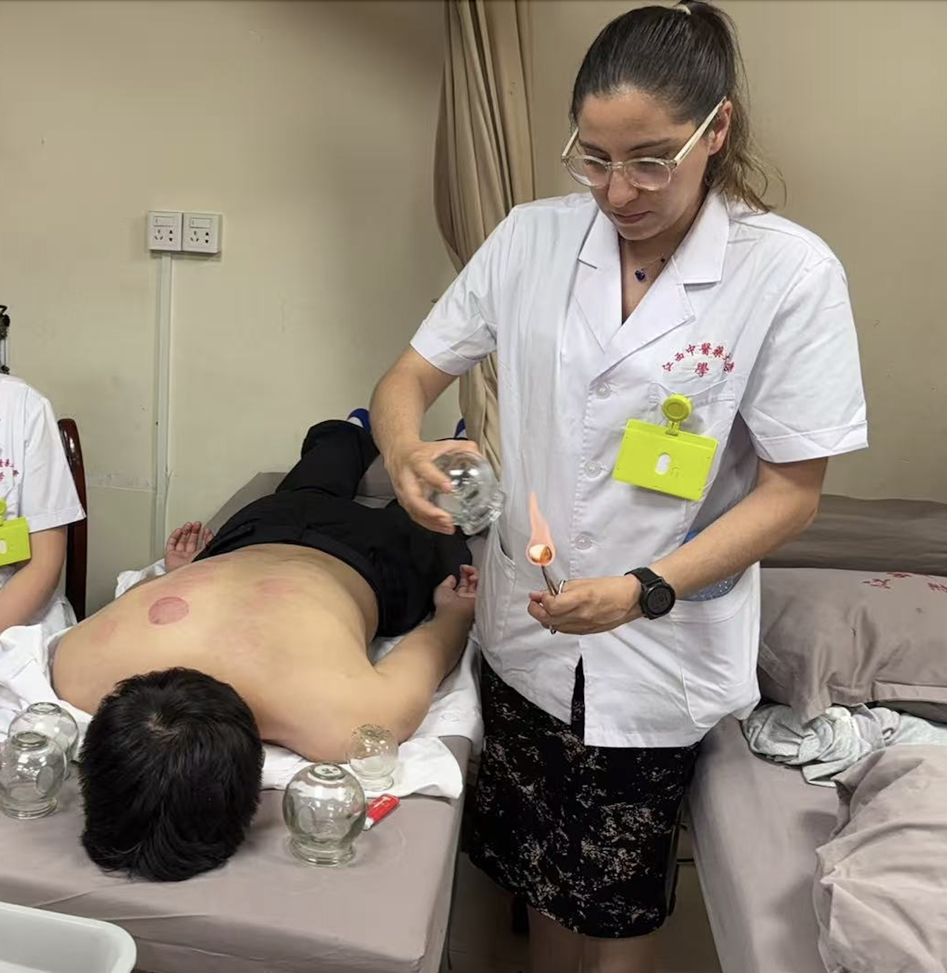 An acupuncturist professional performing a cupping therapy treatment on a patient lying face down in a clinic setting.