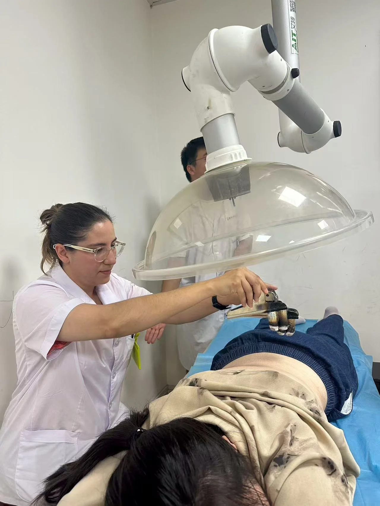 An acupuncturist holding a moxa stick to perform a procedure of moxibustion (heat therapy) on a patient lying on a bed in a hospital room.