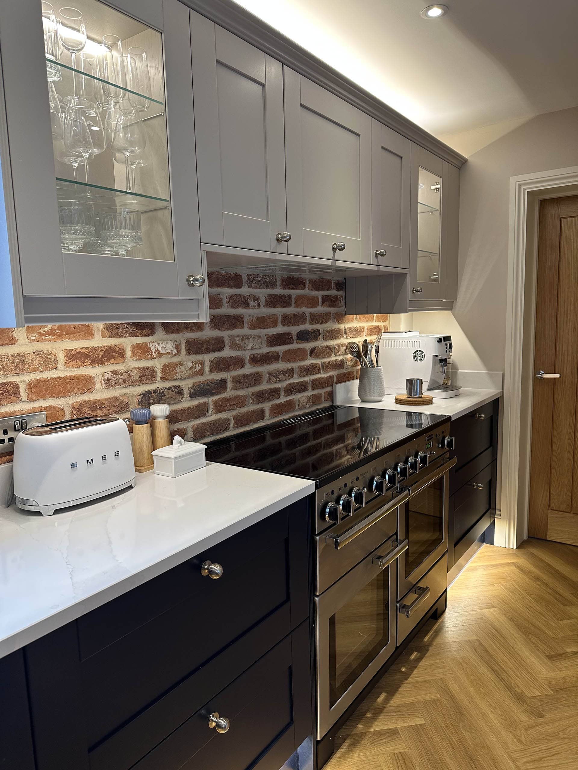 Modern kitchen with gray cabinets, brick backsplash, and white countertops. Features a stainless steel stove, a toaster, and various kitchen utensils.
