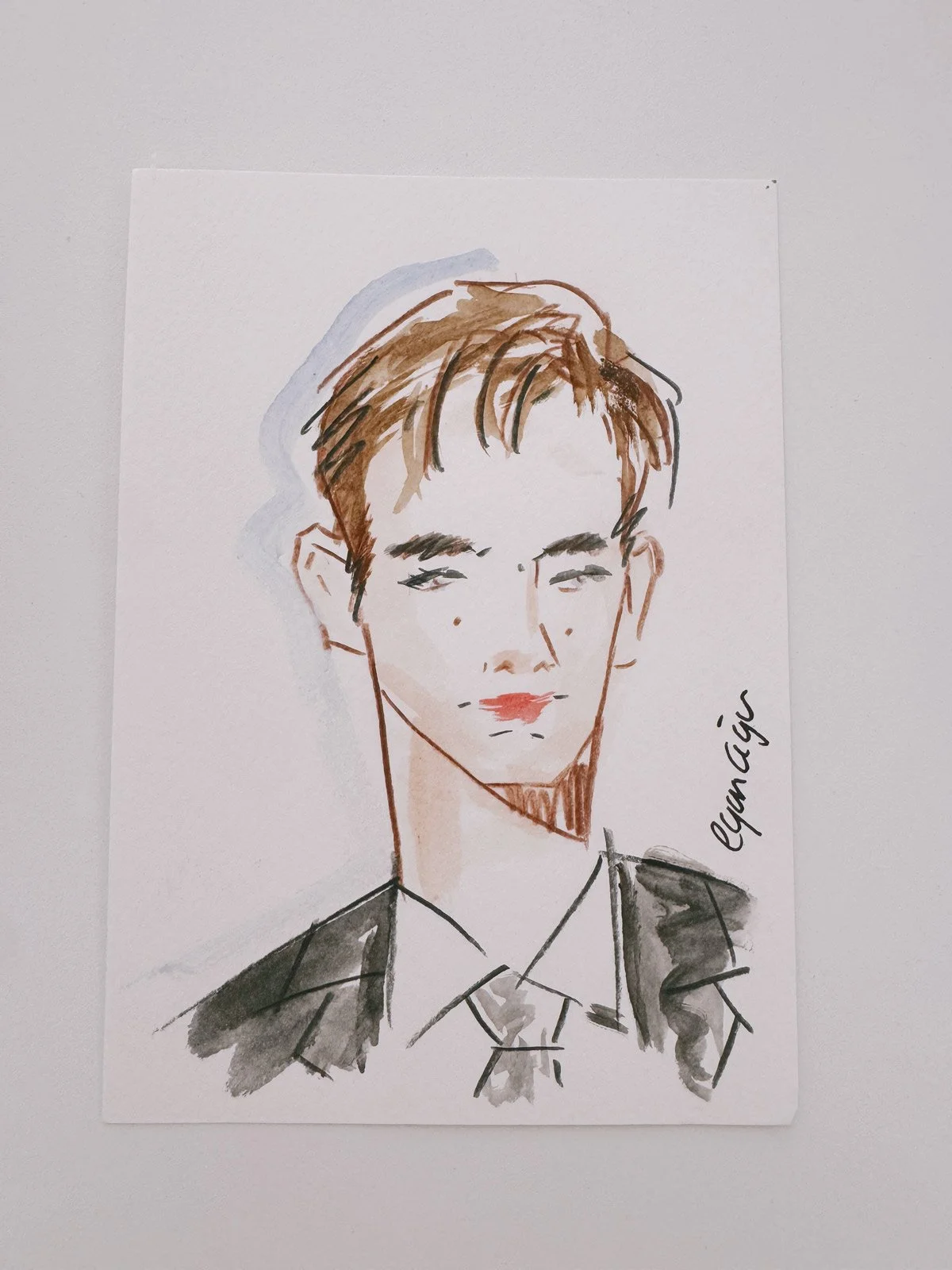 A hand-drawn portrait of a young man with light skin, brown hair, and red lipstick, wearing a suit and tie, signed by EGARCIGU