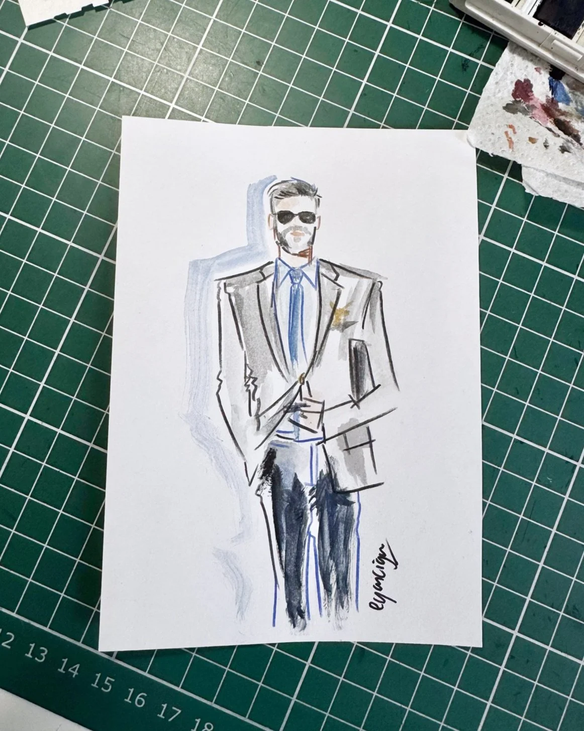 A watercolor fashion illustration of a man in a tan suit, blue shirt, and tie, wearing sunglasses, with one hand in his pocket, signed by the artist Egarcigu