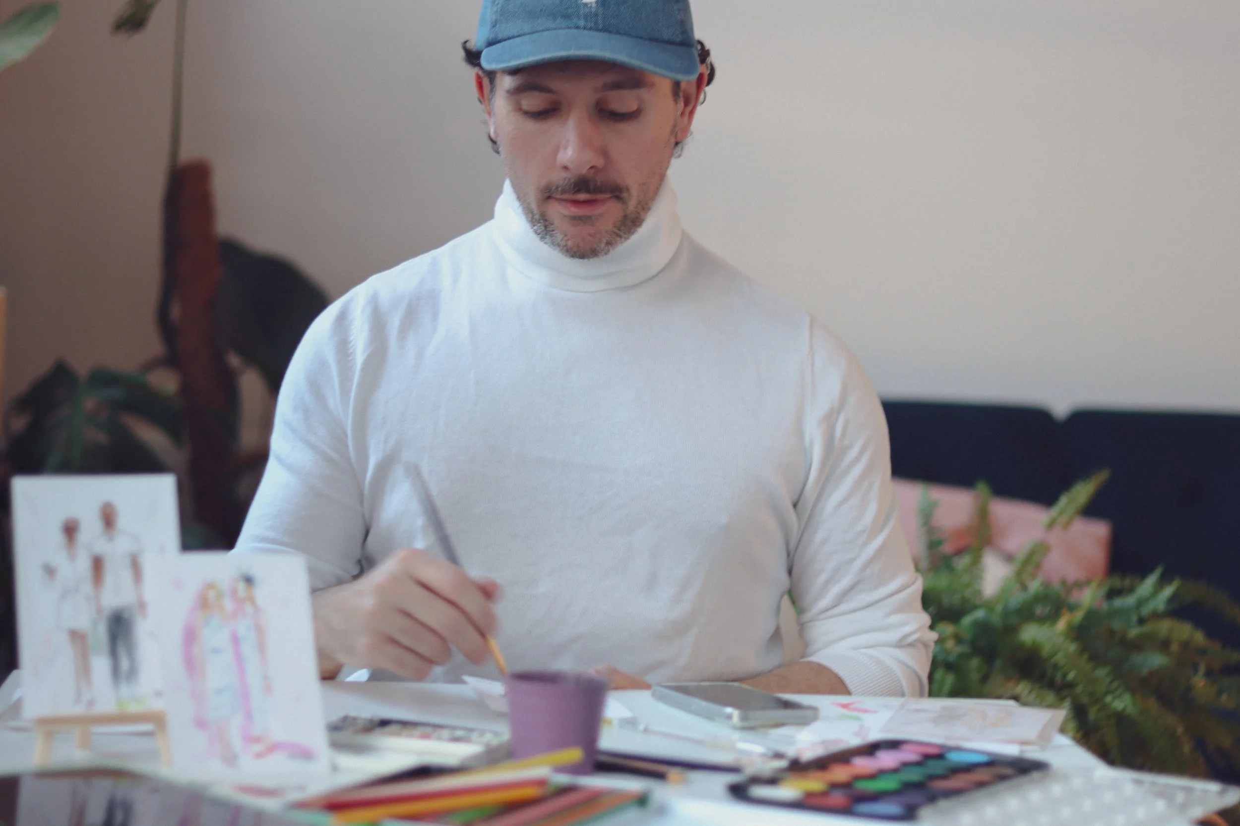 Eduard Illustrates sitting at a table with art supplies, painting a watercolor pictures at an event.