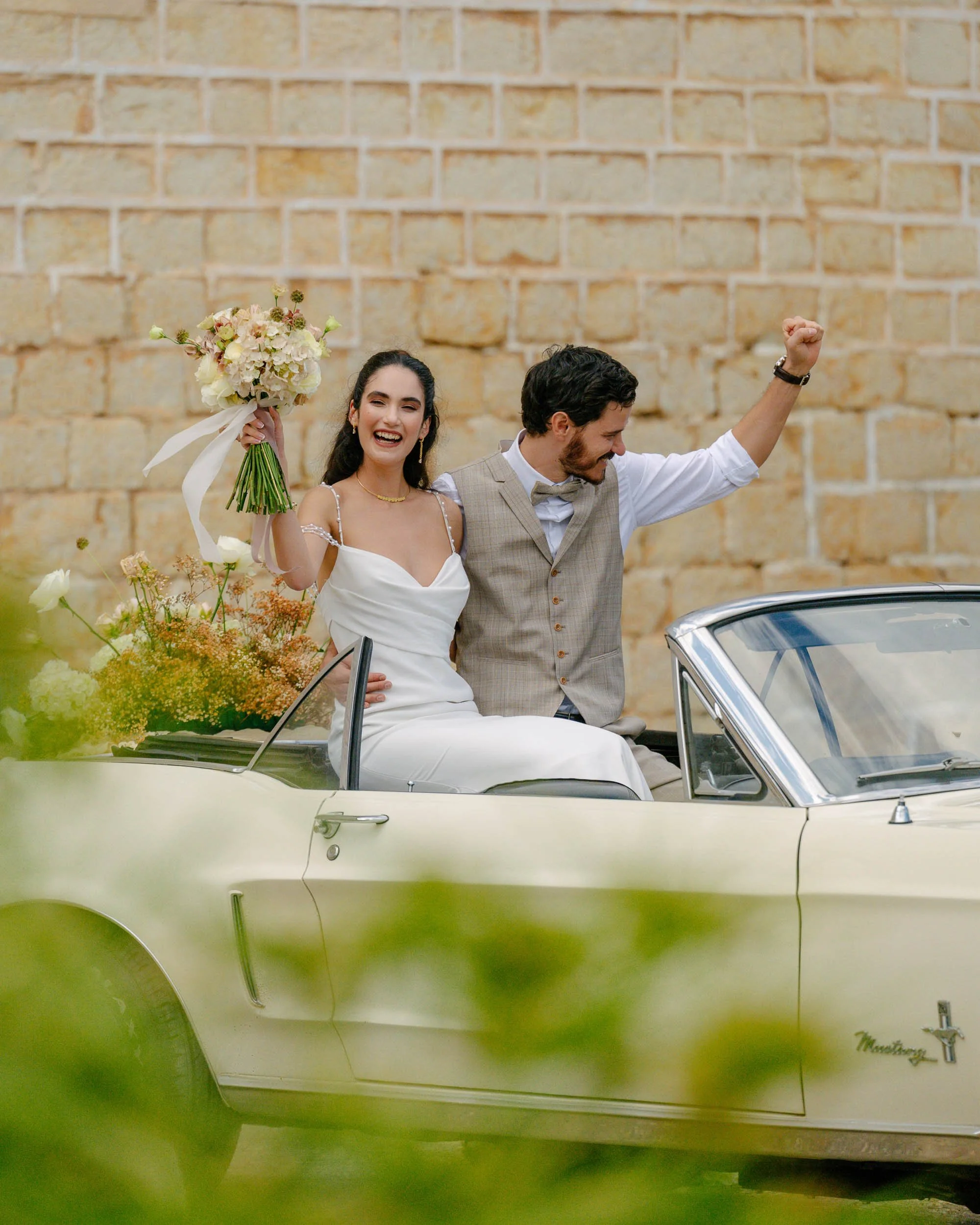 Editorial wedding moment with bride and groom celebrating by a vintage convertible – modern destination wedding photography by Studio Aelina