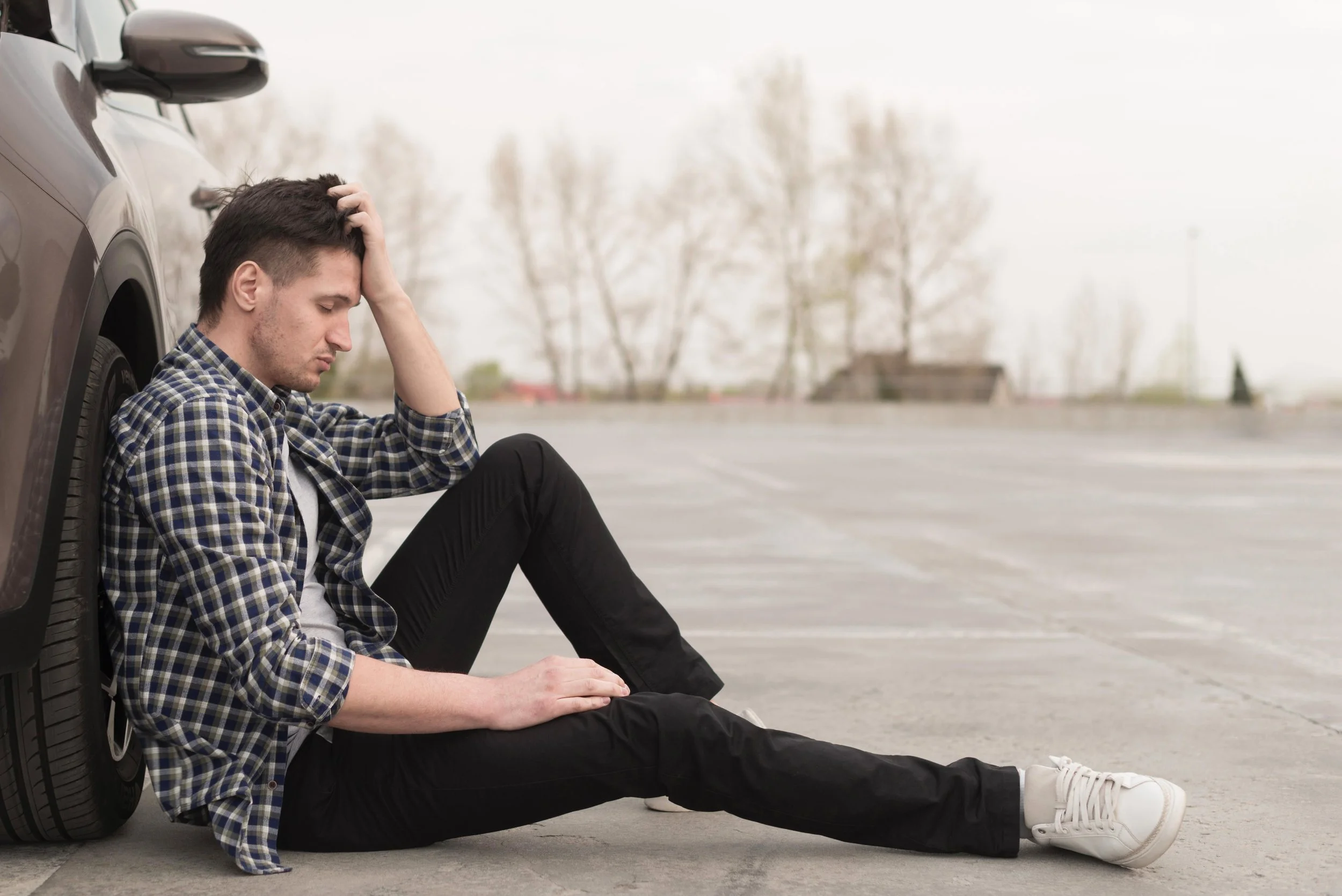 Upset man sitting beside his broken down vehicle