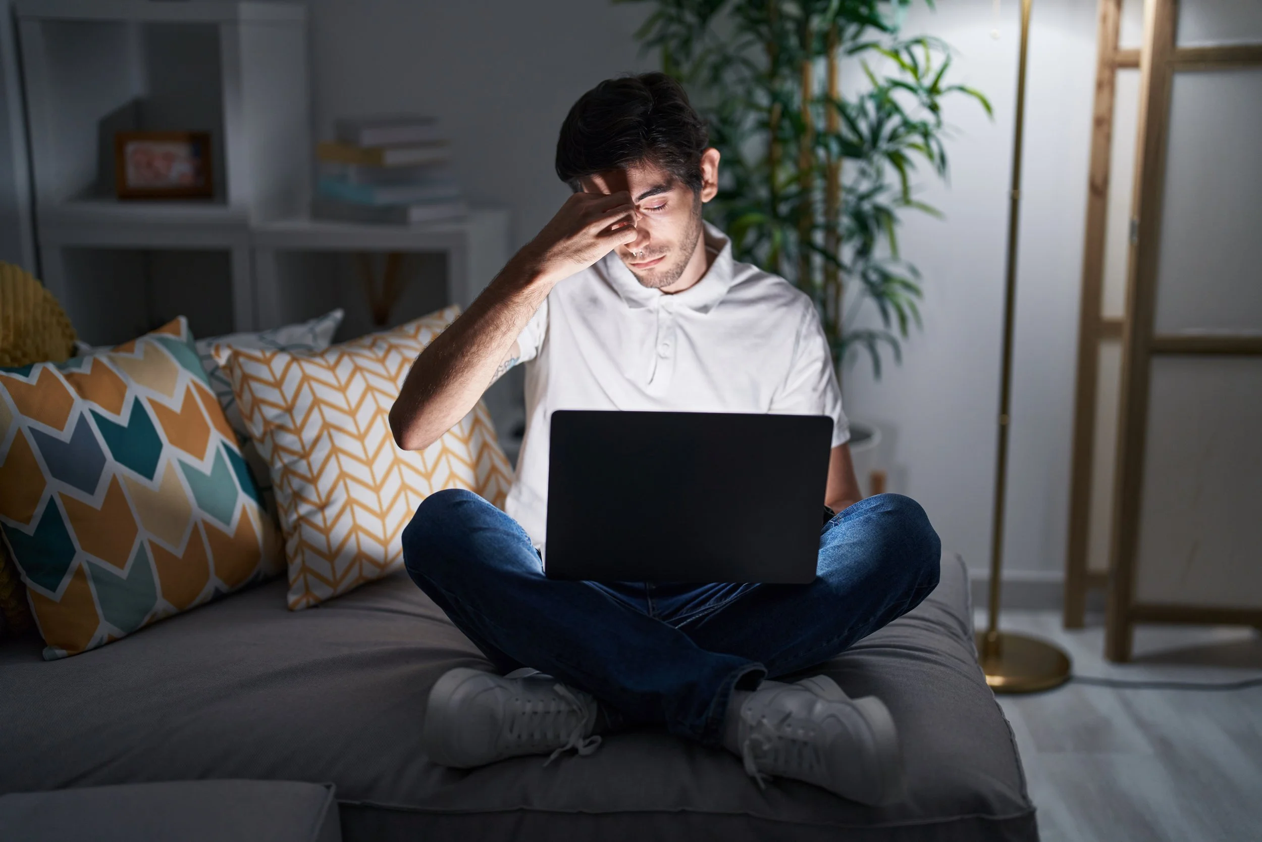 Young man using laptop late at night feeling frustrated