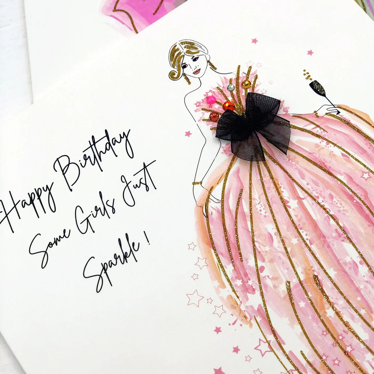Birthday card with a fashion illustration of a woman wearing a pink gown, adorned with a black bow and colorful embellishments, alongside handwritten message.