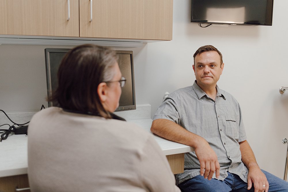 A man and a woman sitting and talking in a medical office or clinic.