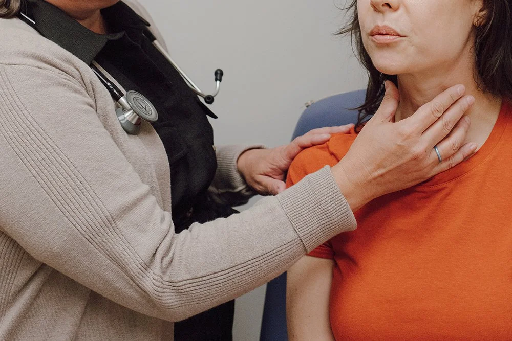 A healthcare professional examines a woman's throat, holding her chin and neck during a medical consultation.