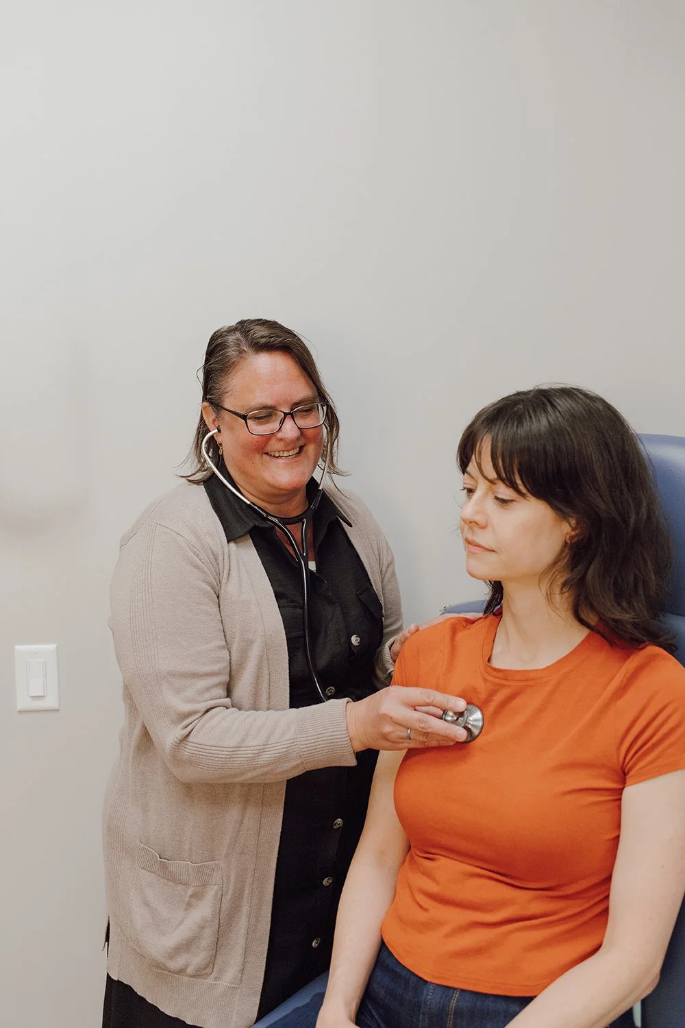 A healthcare professional using a stethoscope on a woman patient in a medical examination room.