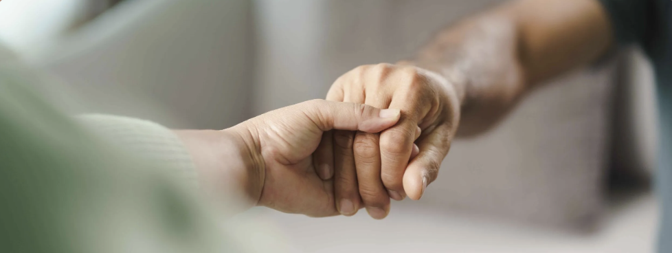 Two people shaking hands, one appears to be older with a darker skin tone and the other younger with a lighter skin tone.