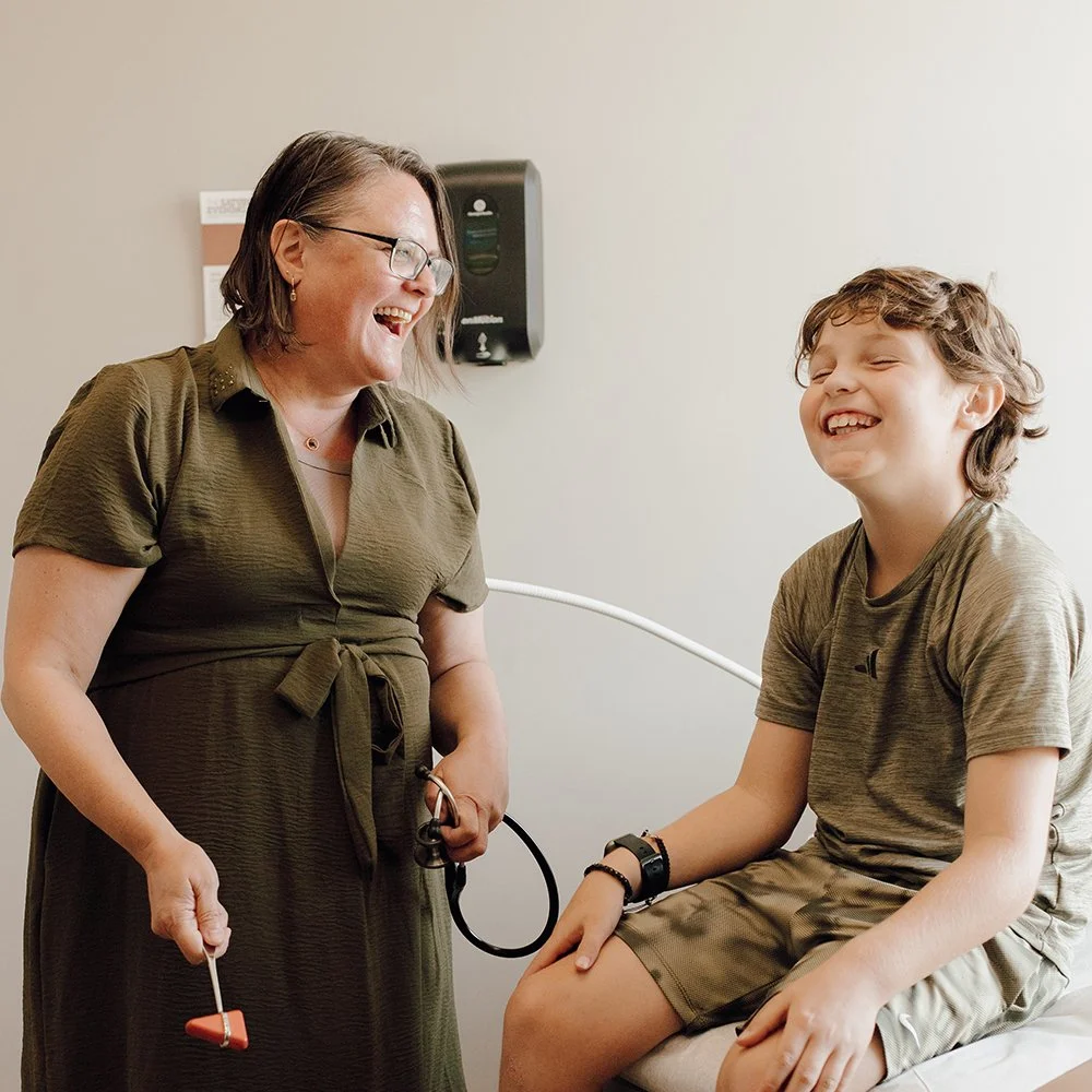A woman and a young boy in a doctor's office, both laughing and smiling during a medical check-up.