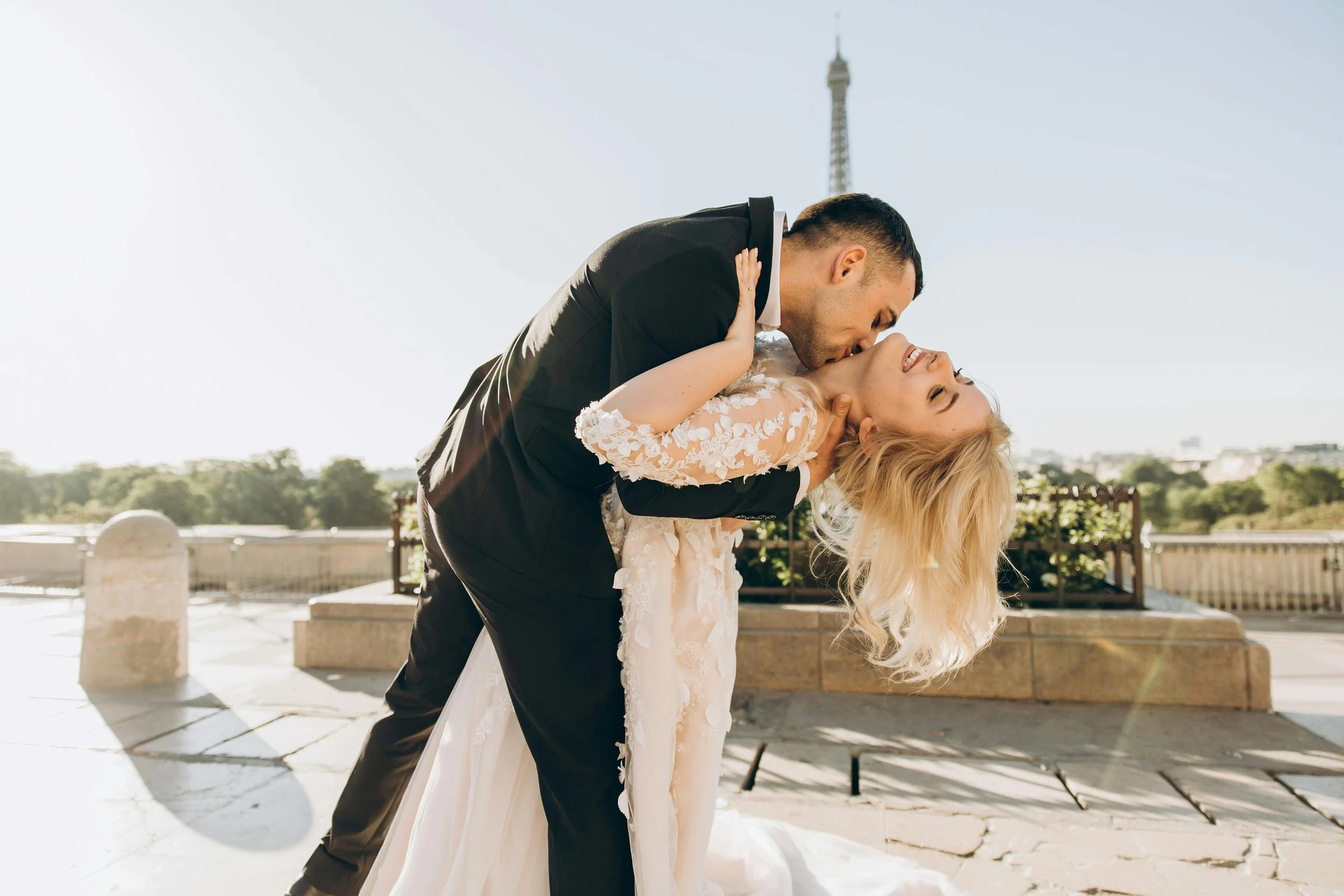 A bride and groom sharing a dance outdoors in daylight, with the Eiffel Tower visible in the background.
