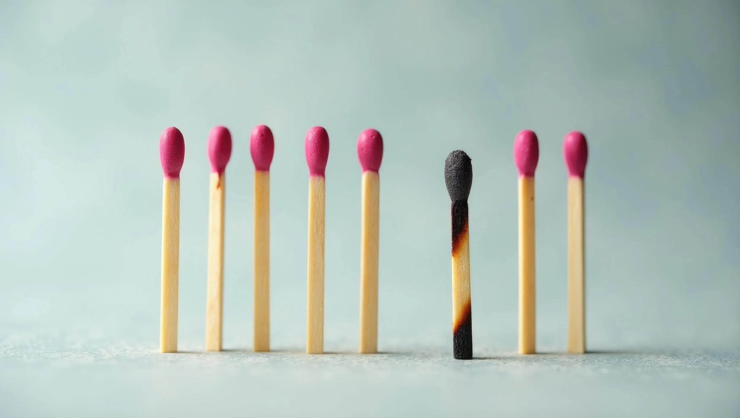 Sieben unbenutzte rosa Streichhölzer und ein abgebranntes Streichholz.