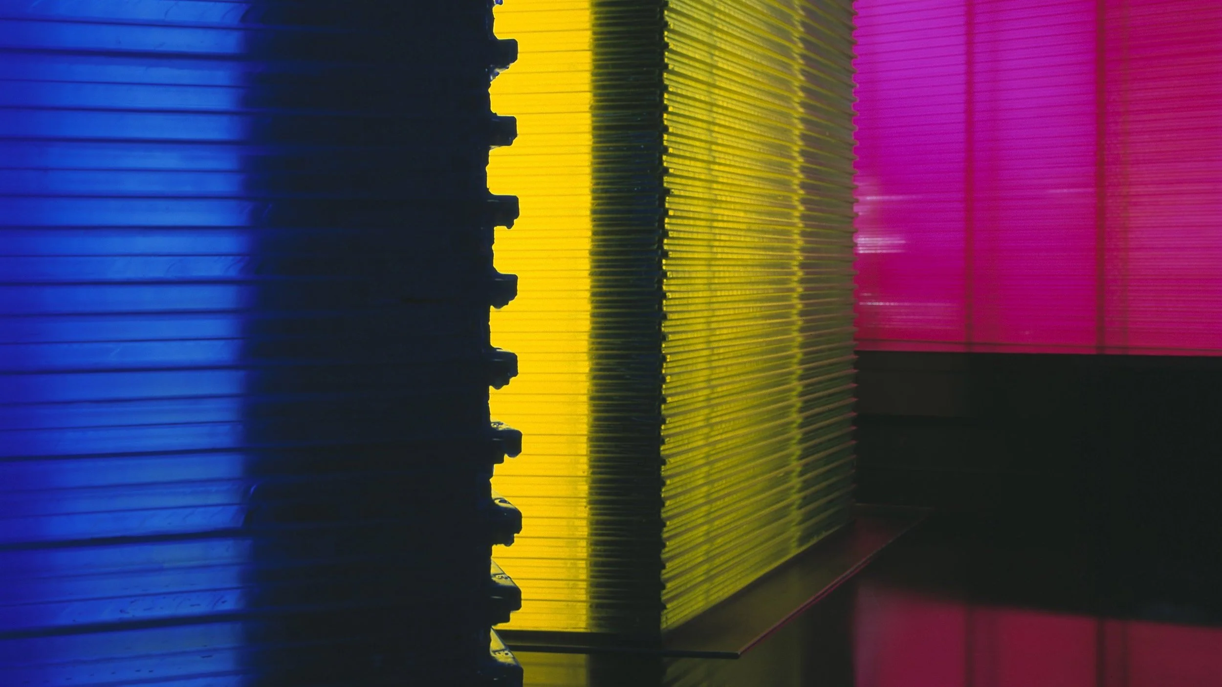 Stacked colorful transparent acrylic sheets in blue, yellow, and pink illuminated by backlighting.