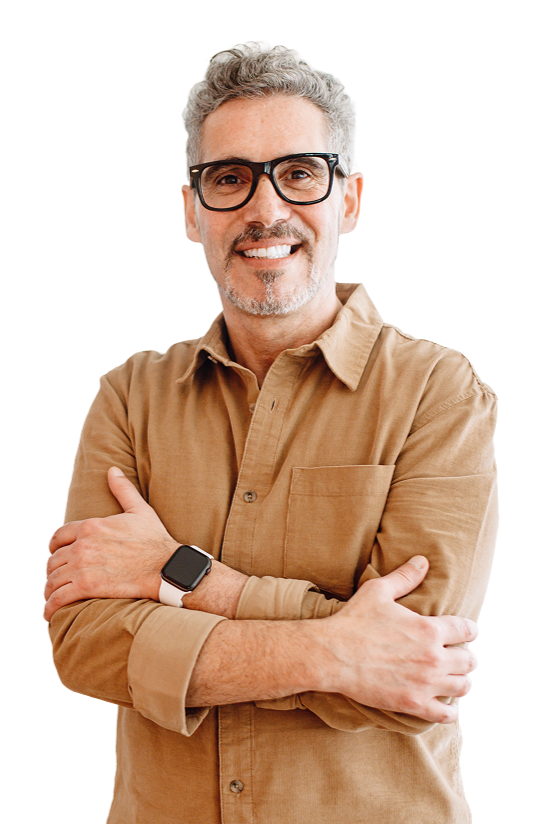 A middle-aged man with gray hair, glasses, and a beard smiling, wearing a tan button-up shirt with sleeves rolled up, and a smartwatch on his left wrist. He is crossing his arms and standing confidently.