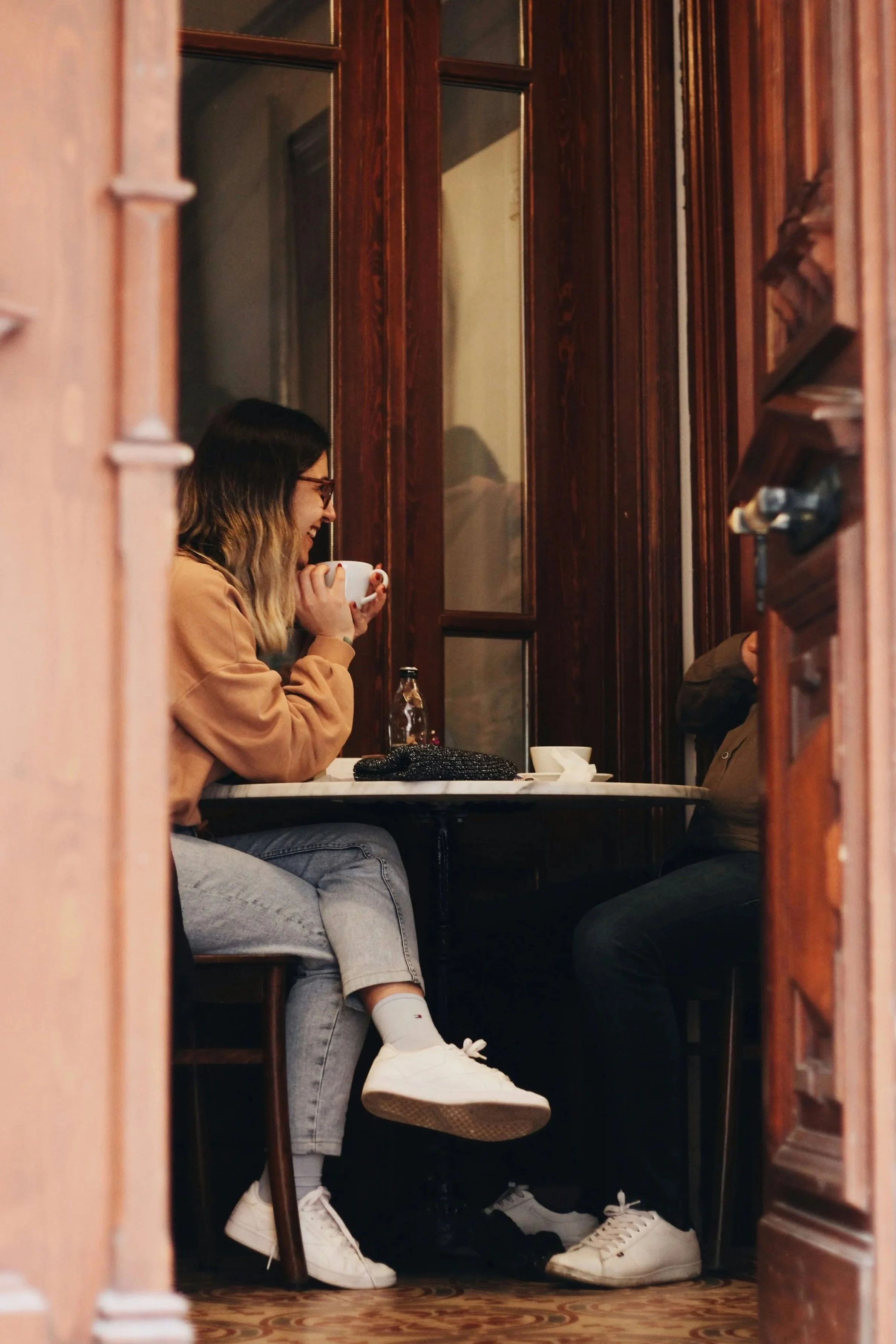 Two people seated at a restaurant table, with one woman holding a white coffee cup in a cozy wood-paneled booth.