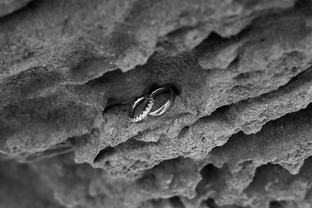 Two wedding rings, one with diamonds, resting on a rough, textured stone surface.