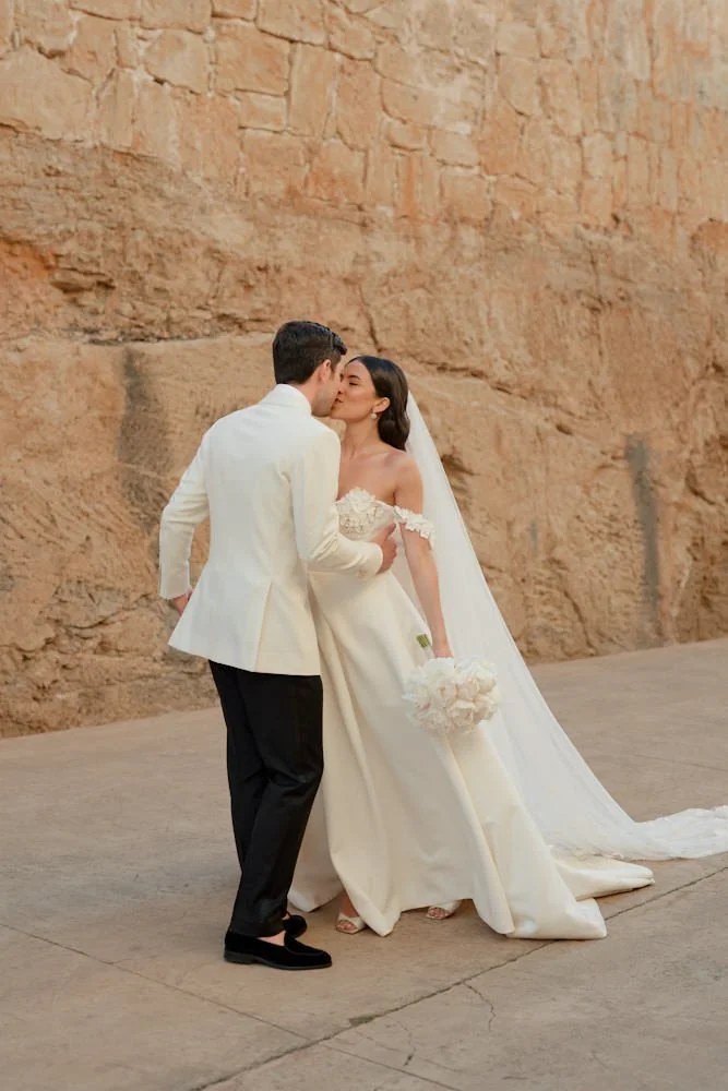 Couple in wedding attire sharing a kiss against a rocky outdoor background.