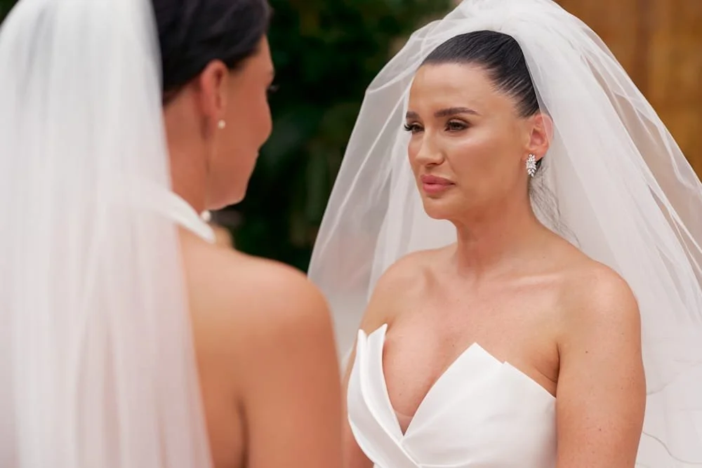 A woman in a wedding dress with a veil looks emotional during a wedding ceremony.