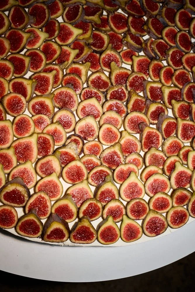 A large tray filled with halved figs showing their red interior and greenish-brown outer skin.