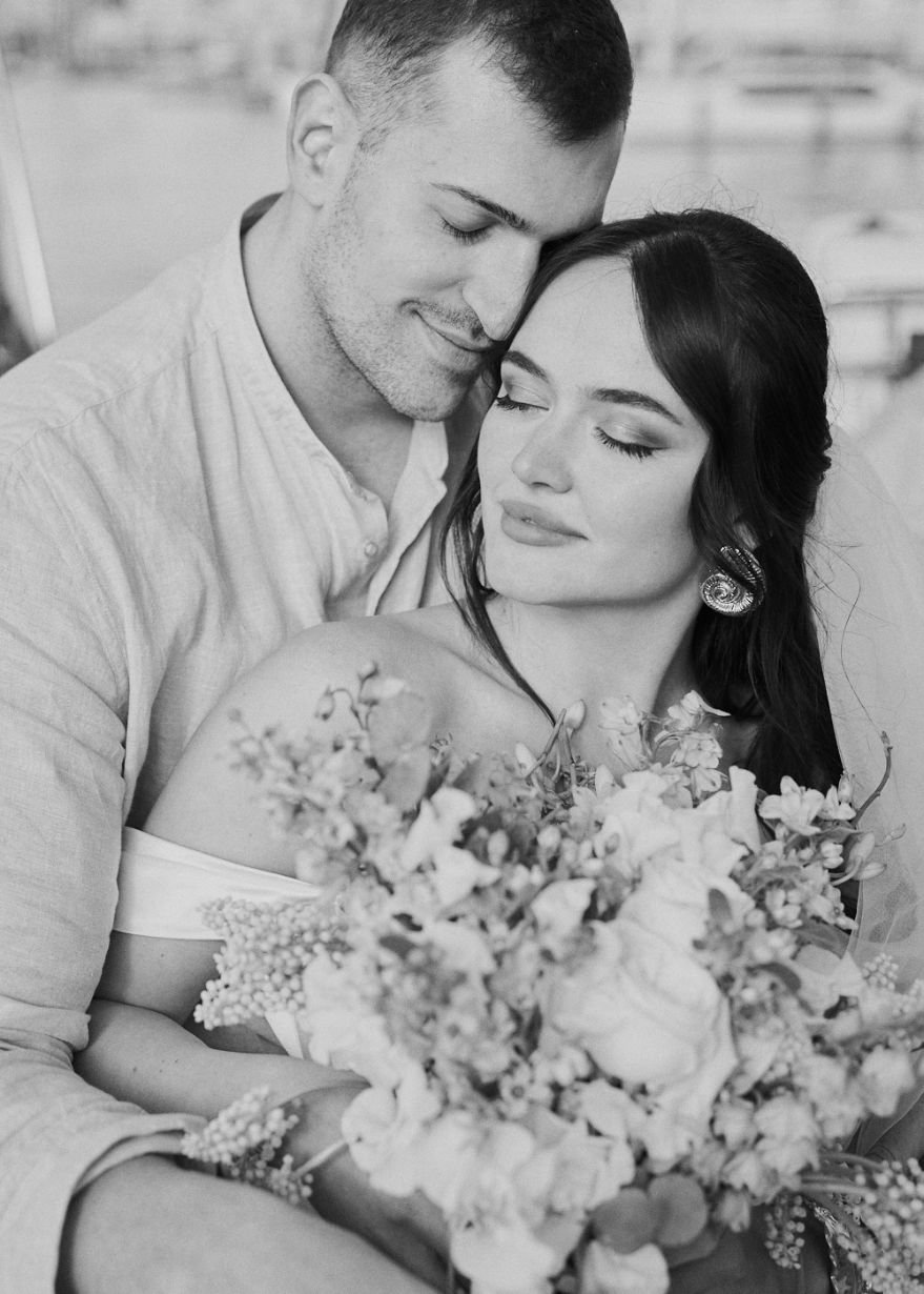 Black and white photo of a bride and groom embracing, with the woman holding a bouquet of flowers.