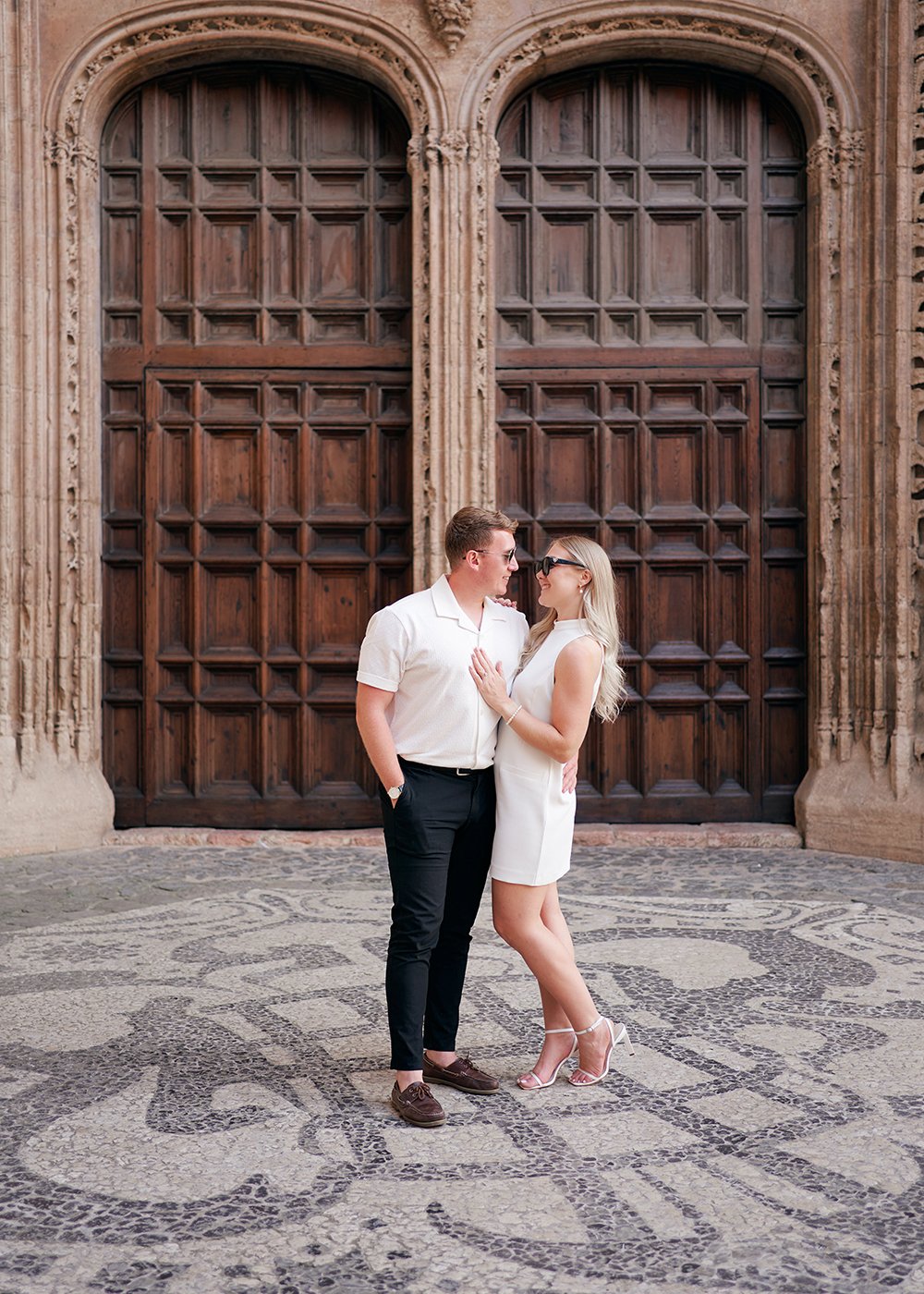 Couple in front of ornate wooden doors, embracing and smiling.