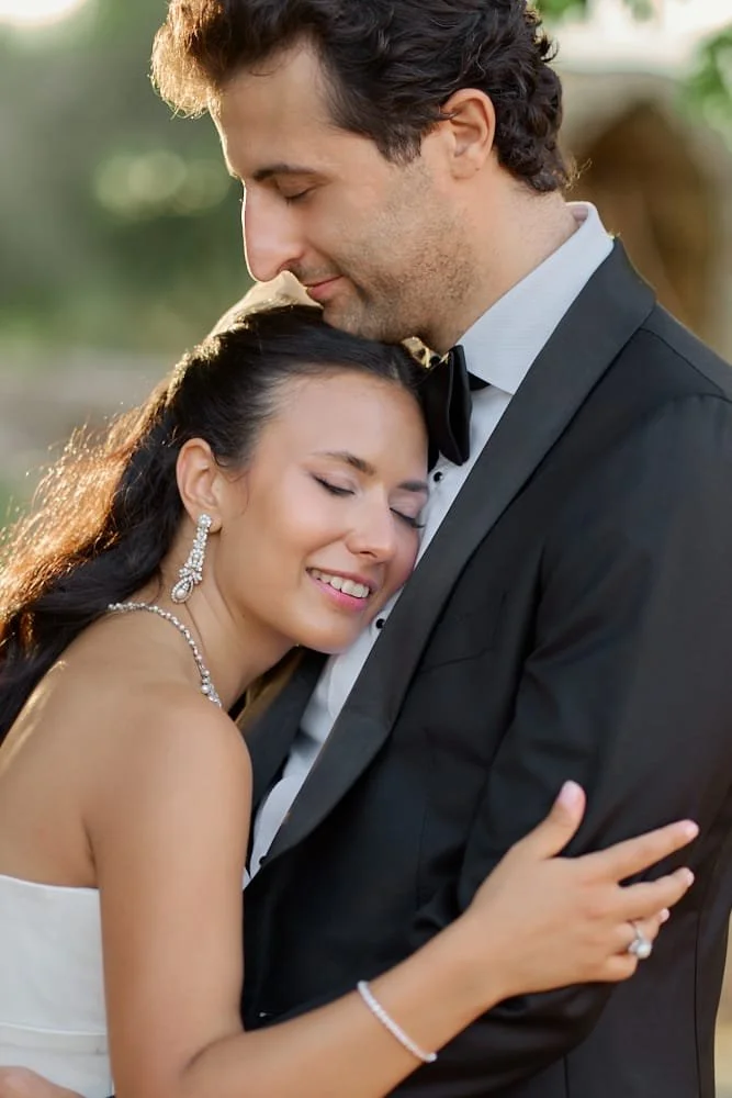 A happy couple dressed in wedding attire, embracing outdoors during sunset.