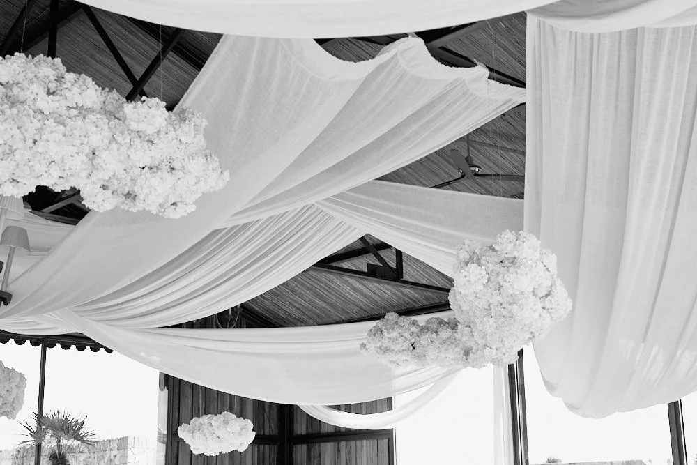 Decorative ceiling with white draped fabric and large white floral arrangements.