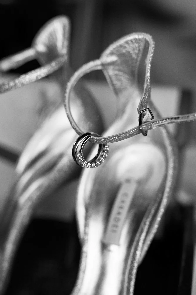 A diamond engagement ring hanging on a glittered, open-toe high-heeled shoe, both placed on a decorative surface.