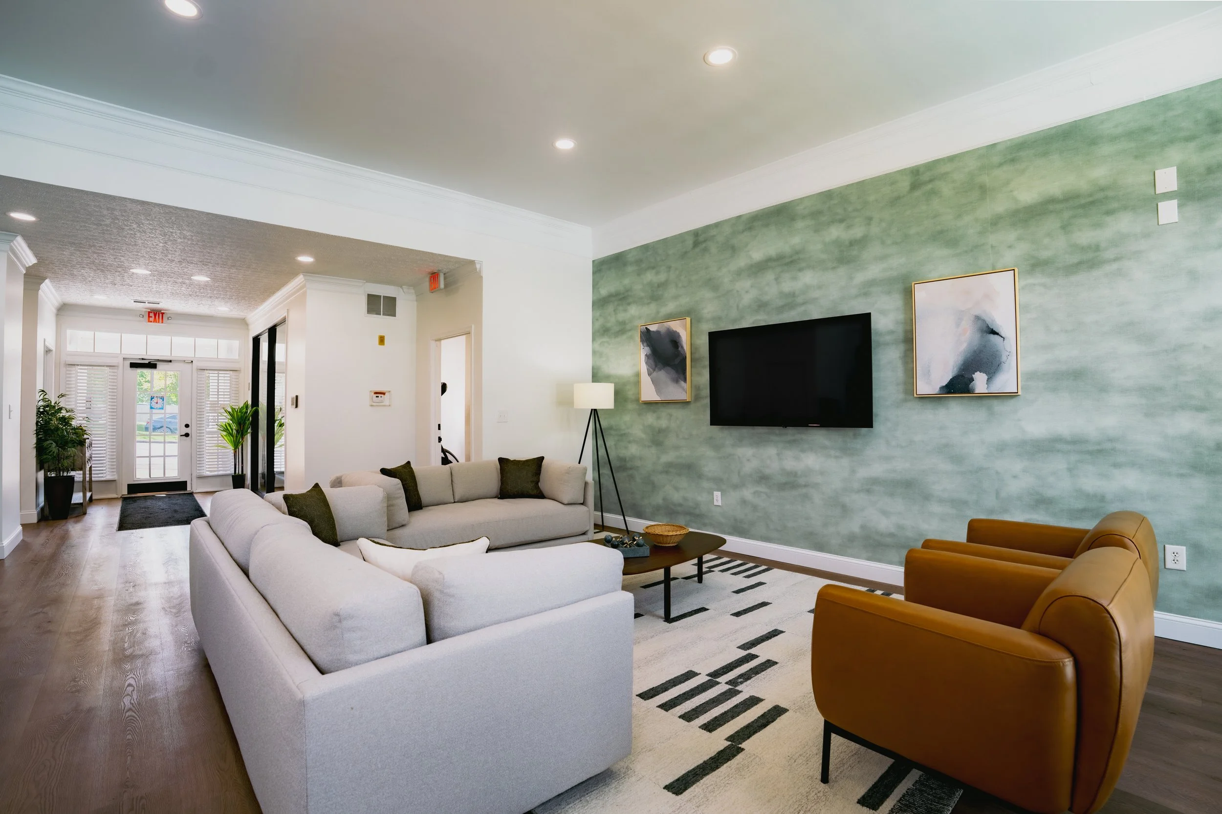 Living room with white sofas, brown armchairs, a black and white striped rug, and a green textured accent wall with wall art and a mounted TV.