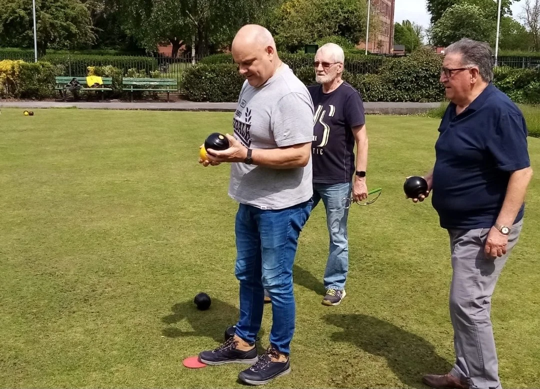 Three men playing bocce on a grassy field in a park.